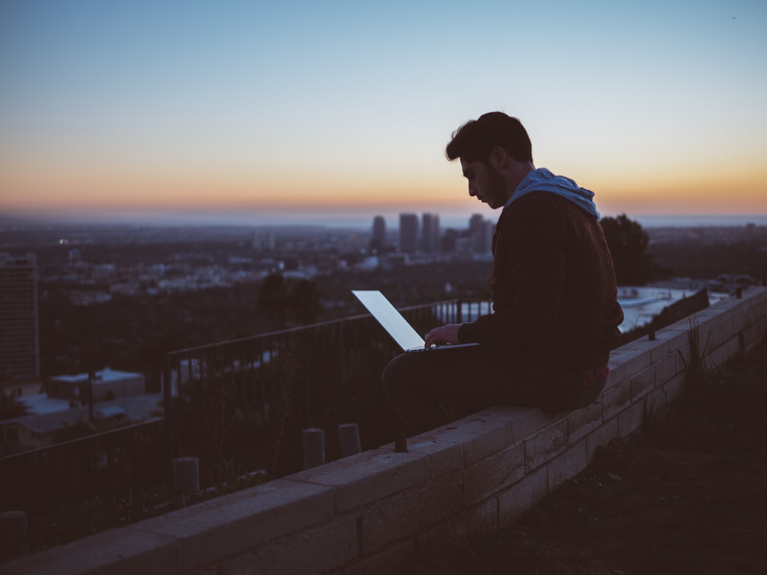 man sitting on ledge with laptop